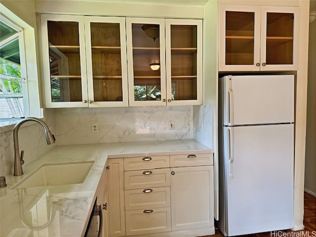 kitchen with light stone counters, tasteful backsplash, freestanding refrigerator, and a sink