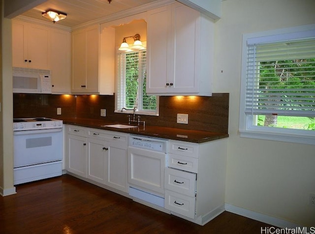 kitchen featuring a sink, white appliances, dark countertops, and a wealth of natural light