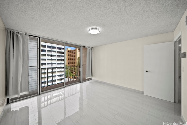 empty room with expansive windows, a textured ceiling, and baseboards