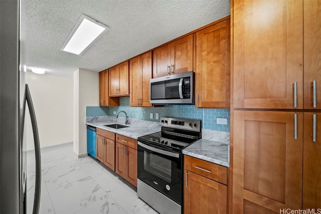 kitchen featuring a sink, marble finish floor, appliances with stainless steel finishes, light stone countertops, and brown cabinetry