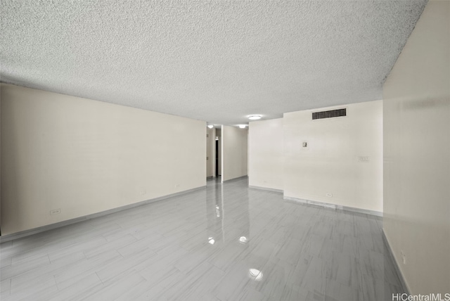 spare room with visible vents, a textured ceiling, and baseboards