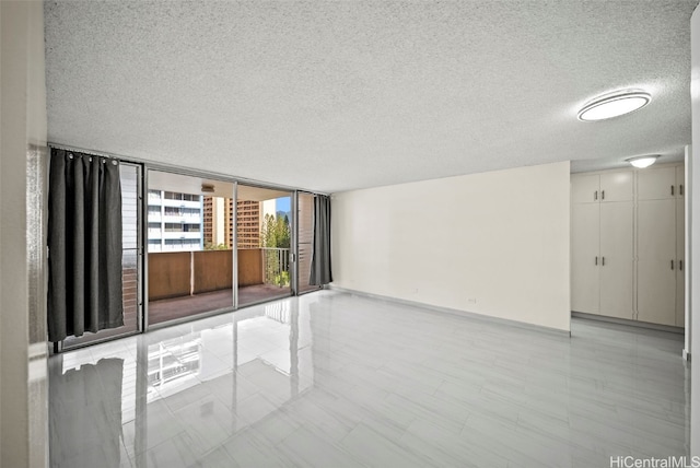 spare room featuring floor to ceiling windows, a textured ceiling, and baseboards