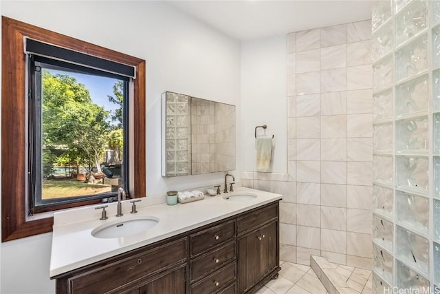 full bathroom with a walk in shower, double vanity, a sink, and tile walls