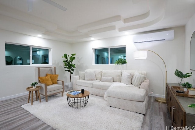 living room featuring recessed lighting, wood finished floors, baseboards, a wall mounted AC, and a tray ceiling