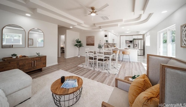 living area featuring baseboards, visible vents, light wood-style flooring, ceiling fan, and a raised ceiling