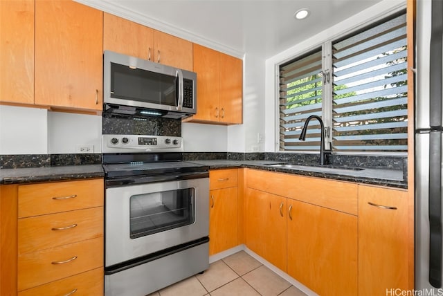 kitchen featuring light tile patterned floors, stainless steel appliances, a sink, brown cabinetry, and dark stone countertops