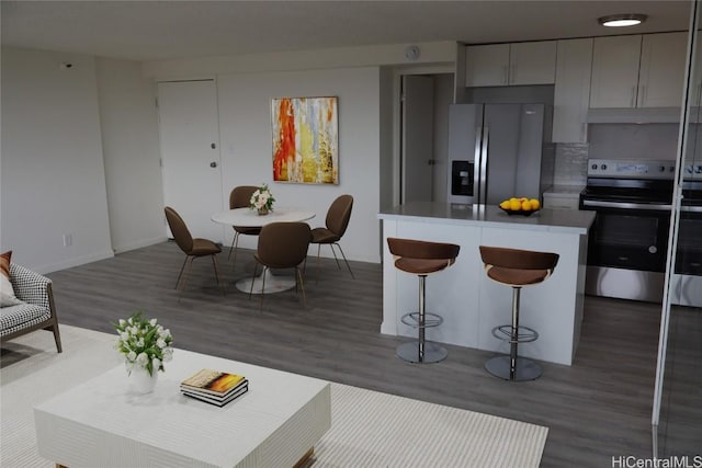 kitchen featuring under cabinet range hood, stainless steel appliances, dark wood-style flooring, gray cabinets, and a center island