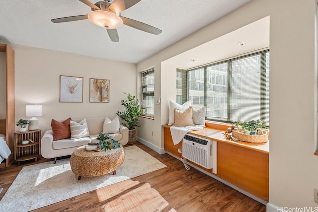 sitting room with an AC wall unit, light hardwood / wood-style floors, and ceiling fan