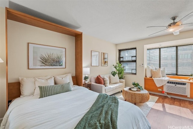 bedroom with ceiling fan, wood-type flooring, a wall mounted AC, and a textured ceiling