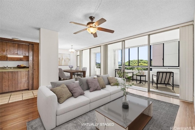 living room with ceiling fan, a wall of windows, wood finished floors, and a textured ceiling