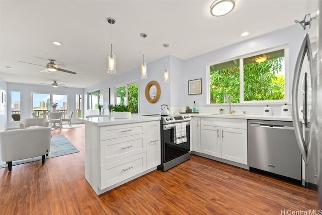 kitchen with stainless steel appliances, light countertops, open floor plan, white cabinets, and a sink