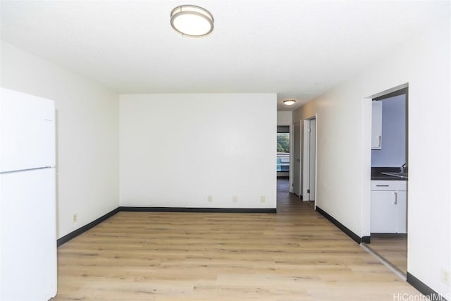 spare room with light wood-type flooring, a sink, and baseboards