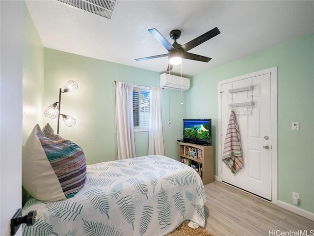 bedroom with visible vents, light wood-style flooring, a wall mounted AC, ceiling fan, and baseboards