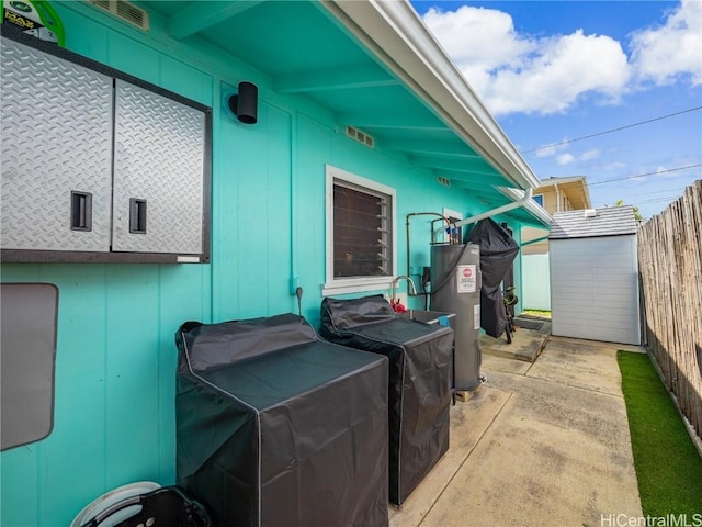 view of patio / terrace featuring an outbuilding, a storage unit, fence, and electric water heater