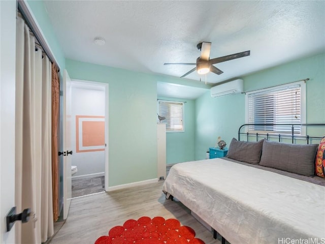 bedroom featuring a textured ceiling, ceiling fan, baseboards, a wall mounted AC, and light wood-type flooring