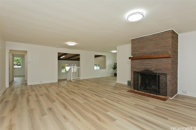 unfurnished living room featuring light wood-type flooring, a healthy amount of sunlight, baseboards, and a tile fireplace