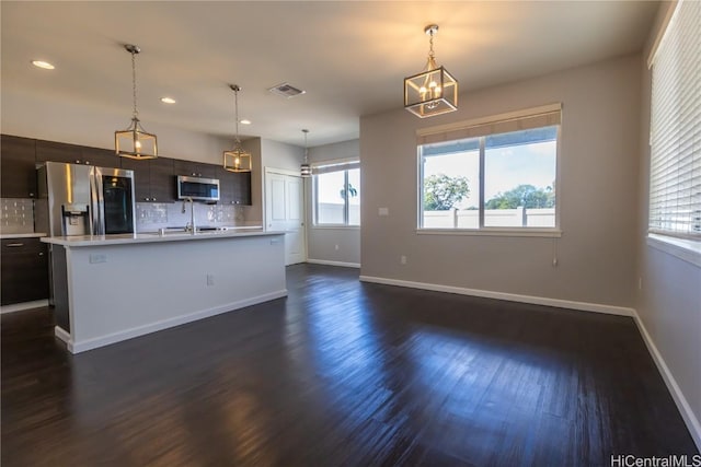 kitchen featuring stainless steel appliances, visible vents, light countertops, a center island with sink, and pendant lighting