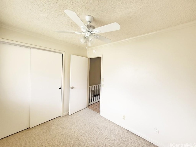 unfurnished bedroom featuring light carpet, a ceiling fan, ornamental molding, a textured ceiling, and a closet