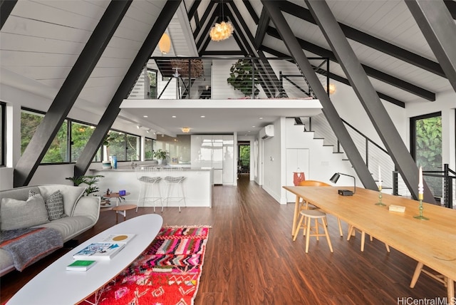 living area with dark wood-style floors, beamed ceiling, a wall unit AC, and a healthy amount of sunlight