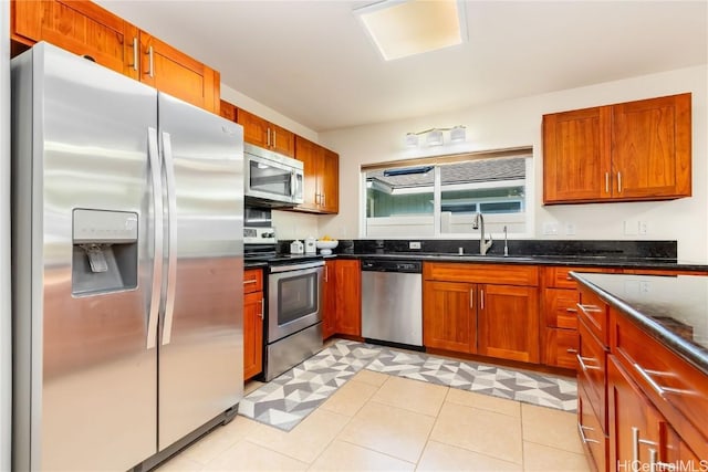 kitchen with appliances with stainless steel finishes, brown cabinets, dark stone countertops, light floors, and a sink