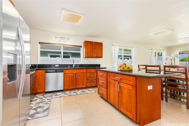 kitchen featuring light tile patterned floors, a kitchen island, dark stone countertops, stainless steel appliances, and a sink