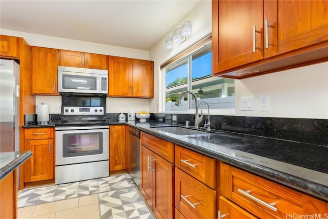 kitchen featuring dark stone counters, stainless steel appliances, brown cabinetry, and a sink