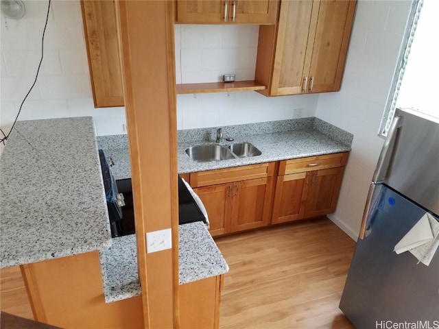 kitchen featuring brown cabinets, open shelves, light wood-style flooring, freestanding refrigerator, and a sink