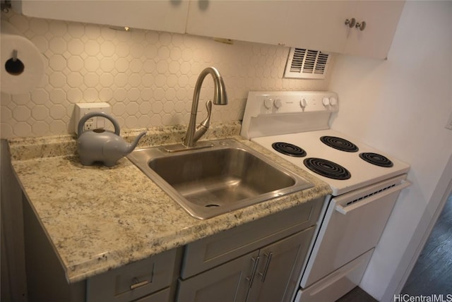 kitchen with light stone counters, a sink, visible vents, backsplash, and white electric range oven