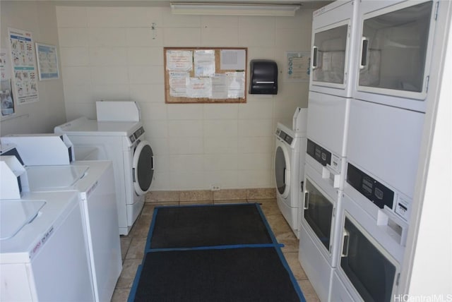 shared laundry area with stacked washer and dryer, light tile patterned floors, tile walls, and independent washer and dryer