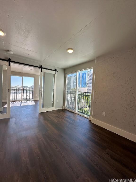 unfurnished room featuring a barn door, baseboards, and dark wood-style flooring