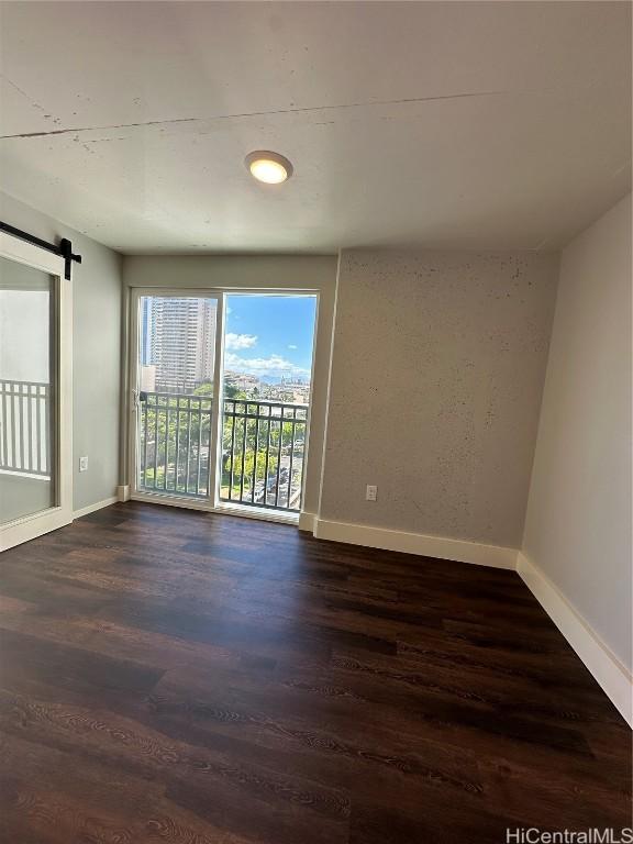 spare room with a barn door, dark wood-style flooring, and baseboards