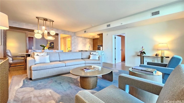 living room featuring visible vents, a notable chandelier, baseboards, and wood finished floors