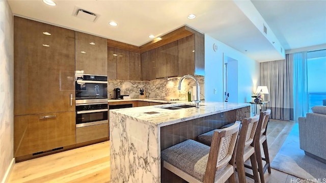 kitchen featuring tasteful backsplash, double oven, a sink, modern cabinets, and a kitchen bar