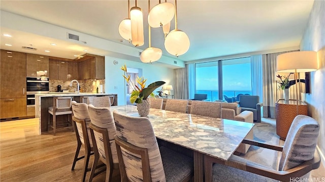 dining space featuring recessed lighting, a water view, visible vents, and light wood-style floors