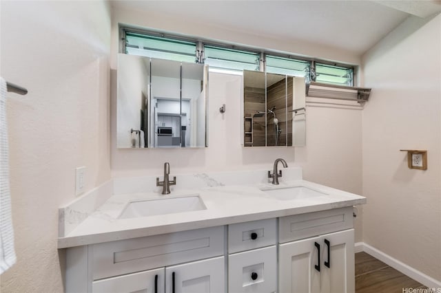 full bathroom with baseboards, wood finished floors, double vanity, and a sink