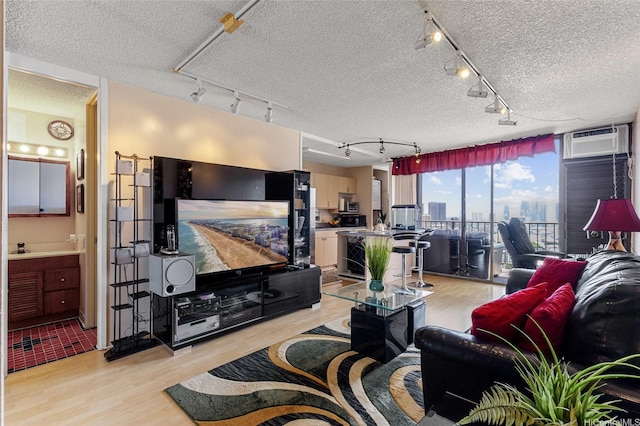 living room with a textured ceiling, track lighting, light wood-style flooring, and a wall unit AC