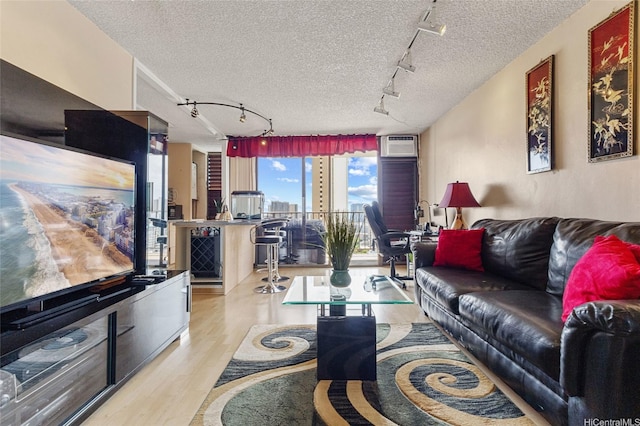 living room with a textured ceiling, an AC wall unit, rail lighting, and wood finished floors