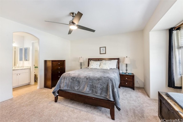 bedroom with arched walkways, light colored carpet, ensuite bath, and ceiling fan