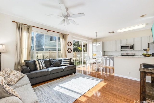 living room with ceiling fan with notable chandelier, wood finished floors, and visible vents