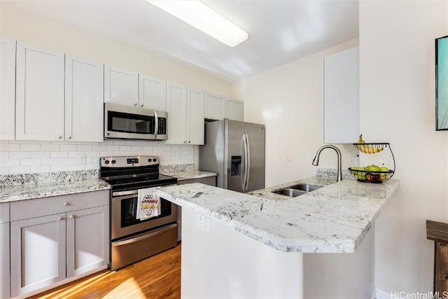 kitchen with a sink, backsplash, stainless steel appliances, a peninsula, and light stone countertops