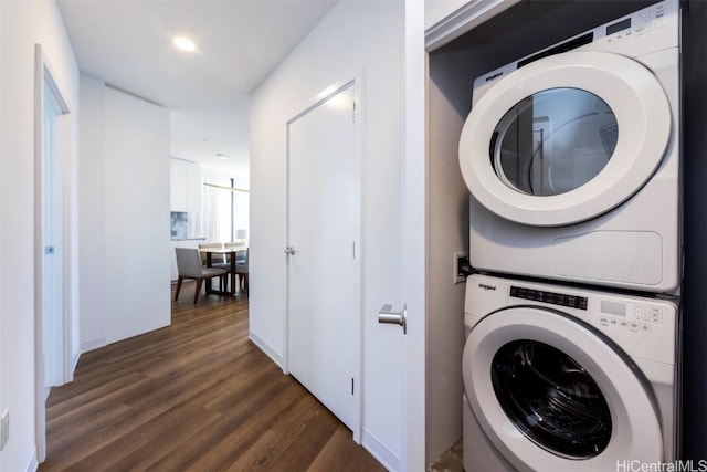 clothes washing area featuring stacked washer and dryer, dark wood finished floors, and laundry area