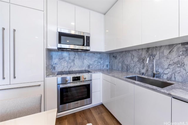 kitchen featuring stainless steel appliances, a sink, white cabinetry, light stone countertops, and modern cabinets