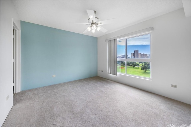 carpeted spare room with a ceiling fan and a city view