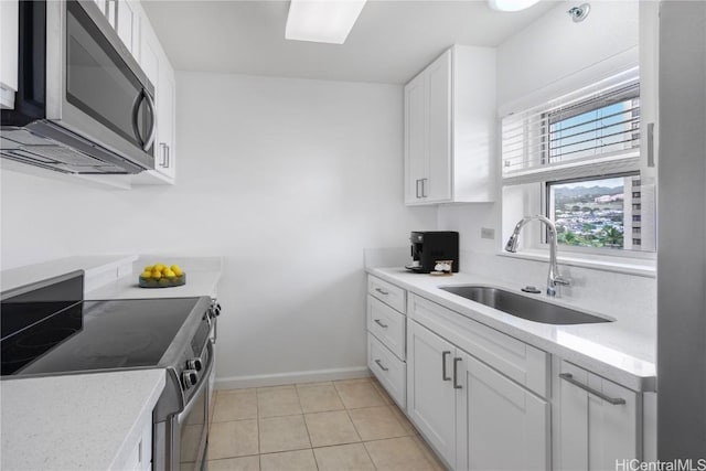 kitchen with light tile patterned floors, stainless steel appliances, light countertops, white cabinetry, and a sink