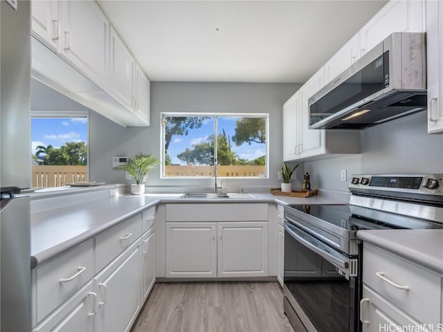 kitchen featuring stainless steel appliances, a sink, white cabinets, light countertops, and plenty of natural light