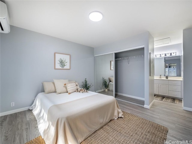 bedroom featuring baseboards, an AC wall unit, a closet, and light wood-style floors