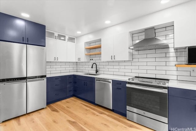 kitchen featuring blue cabinetry, wall chimney range hood, light countertops, stainless steel appliances, and open shelves