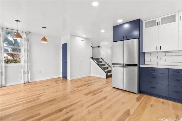 kitchen featuring backsplash, pendant lighting, light countertops, light wood-style flooring, and freestanding refrigerator