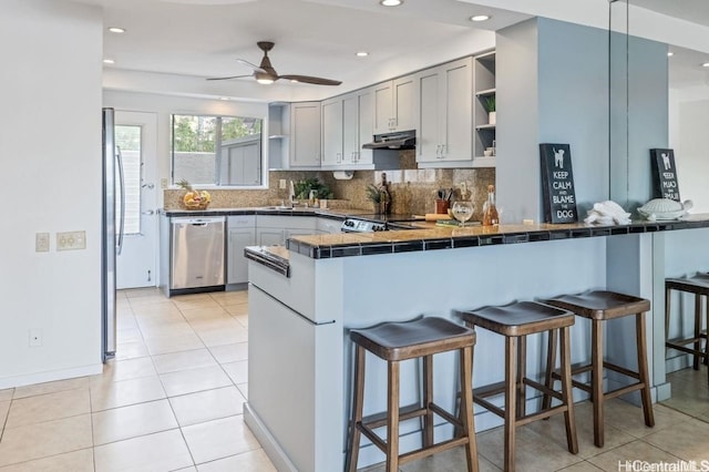 kitchen with open shelves, stainless steel appliances, dark countertops, gray cabinetry, and under cabinet range hood