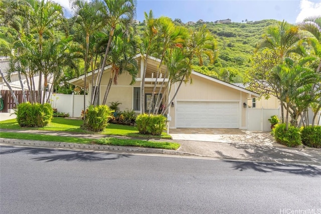 mid-century modern home with a garage, a front lawn, decorative driveway, and fence